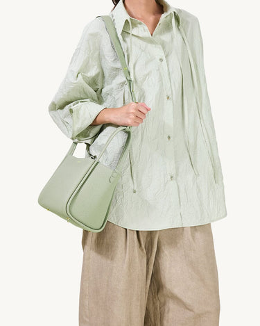 Medium Song Bag in Jade pebbled leather, carried by a person wearing a light green crinkled shirt and tan trousers.