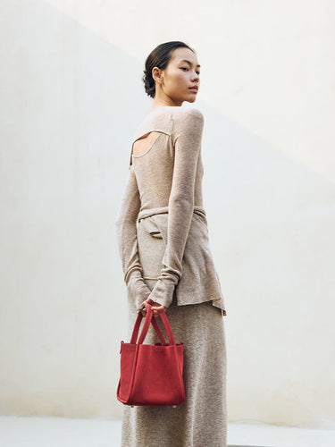 Medium Song Bag in Poppy red nubuck leather, held by a woman in a tan knit outfit.