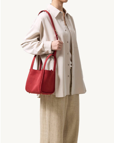 Red medium Song bag carried by a woman wearing a beige oversized shirt and linen pants.