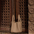 Medium Song Bag in taupe full-grain leather with dual handles against carved wood panels.