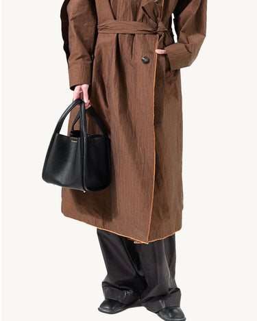 Medium Song Bag in black vegan leather, held by a model wearing a brown coat and black pants.