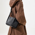 Medium Song Bag in Eco Onyx vegan leather worn by a woman in a brown coat.