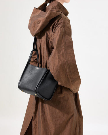 Medium Song Bag in Eco Onyx vegan leather worn by a woman in a brown coat.