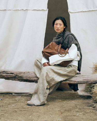Medium Yore Duffle Bag in Sandal. Vegetable-tanned leather, timeless design, held by woman.