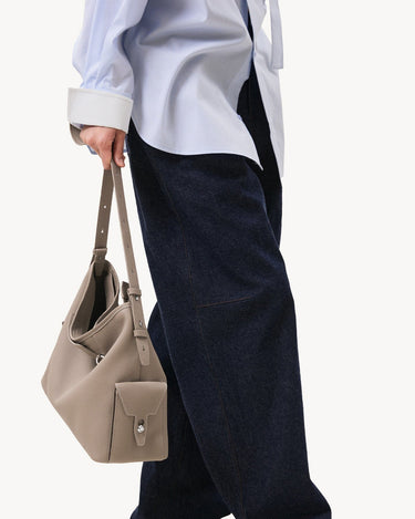 Medium Yore Hobo Bag in Cobble Grain leather, held by a person wearing a blue pinstripe shirt and dark jeans.