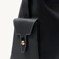 Medium Yore Hobo Bag in Onyx Grain leather with a gold clasp on a flap pocket.