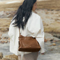 Medium Yore Hobo Bag in Sandal color, made of vegetable-tanned leather, worn by a woman outdoors.