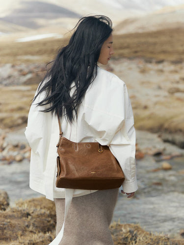 Medium Yore Hobo Bag in Sandal color, made of vegetable-tanned leather, worn by a woman outdoors.