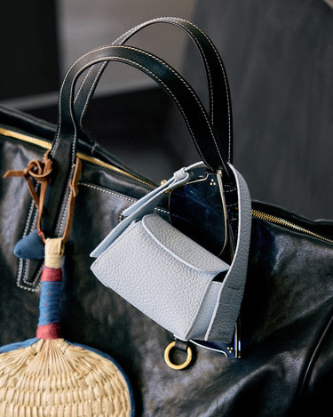 Sky Mini Drippy AirPods Case made of pebbled leather with stainless steel hardware, attached to a large black leather bag.
