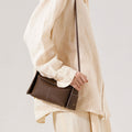 Brown Mini Drippy Roof Bag in textured leather with white stitching, worn by a person in a cream linen outfit.