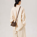 Model from behind wearing a tan linen outfit and a dark brown leather Mini Drippy Roof Bag slung across her shoulder.