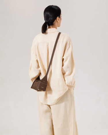 Model from behind wearing a tan linen outfit and a dark brown leather Mini Drippy Roof Bag slung across her shoulder.