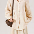 Model wearing a light beige linen shirt and pants, holding a chocolate-colored Mini Drippy Roof Bag with white stitching.