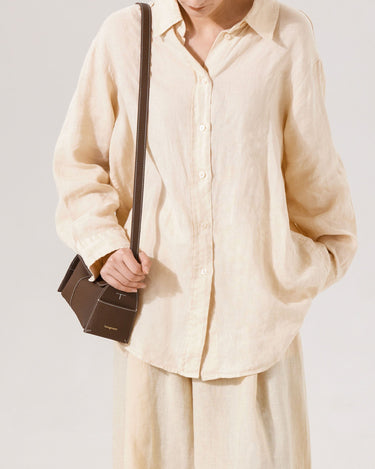 Model wearing a light beige linen shirt and pants, holding a chocolate-colored Mini Drippy Roof Bag with white stitching.