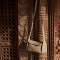 Cobble pebble leather Mini Drippy Roof Bag, structured crossbody with flap closure, against carved wood.