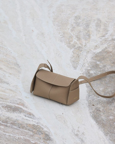 Mini Drippy Roof Bag in Cobble textured leather, with a flap closure and adjustable strap, resting on a marble-like surface.