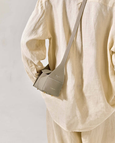 Mini Drippy Roof Bag in Cobble color, a pebbled leather crossbody bag with architectural design, worn with a linen outfit.