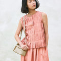 Mini Drippy Roof Bag in Ivory, textured leather crossbody bag with flap, worn with pleated pink outfit.