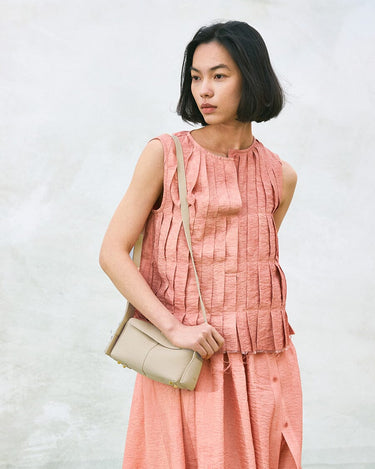 Model wearing peach outfit with ivory Mini Drippy Roof Bag. Textured leather crossbody bag.