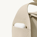 Mini Drippy Roof Bag in ivory pebbled leather with exterior pocket holding white earbuds.