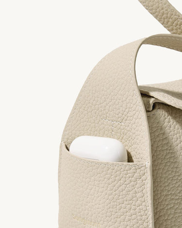 Mini Drippy Roof Bag in ivory pebbled leather with exterior pocket holding white earbuds.