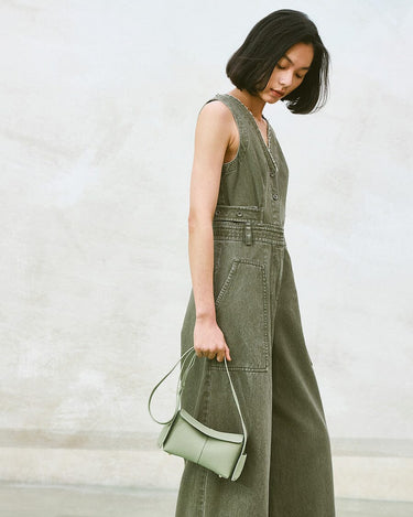Pale green mini drippy roof bag, full-grain leather, with adjustable strap, held by woman in olive green jumpsuit.