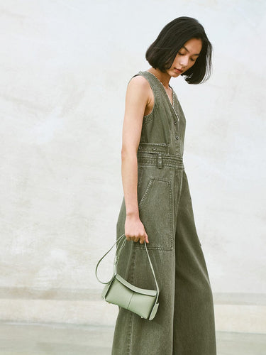 Pale green mini drippy roof bag, full-grain leather, with adjustable strap, held by woman in olive green jumpsuit.