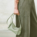 Light green full-grain leather mini drippy roof bag with adjustable strap worn by a person in olive green pants.