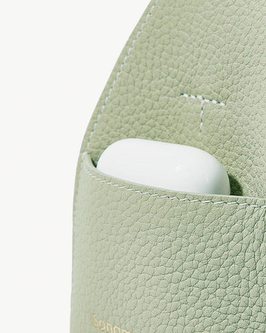 Sage green full-grain leather mini drippy roof bag with white earbuds peeking out.