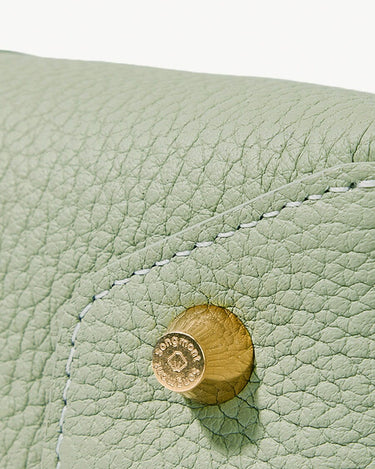 Close-up of light green full-grain leather bag with gold hardware featuring 'Songmont' logo.