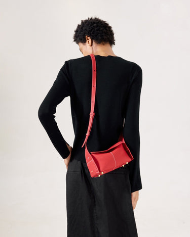 Red full-grain leather mini drippy roof bag with white stitching and gold hardware, worn by a woman.