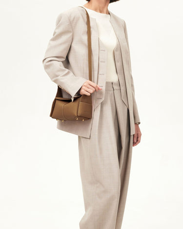 Mini Drippy Roof Bag in Mocha, made of full-grain leather with gold hardware, worn by a model in a beige suit.