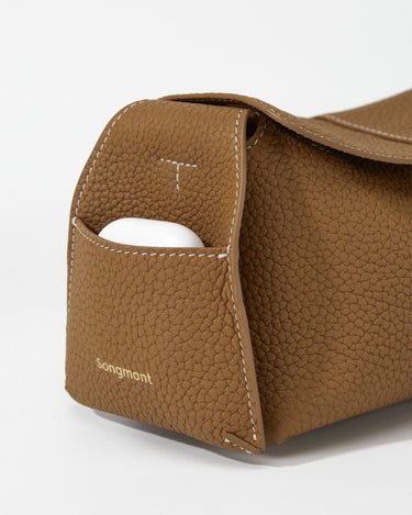 Mini Drippy Roof Bag in Mocha, crafted from textured leather with a convenient front pocket holding white earbuds.