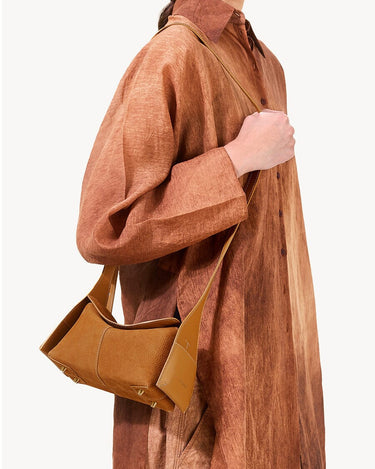Mini Drippy Roof Bag in Sea Buckthorn nubuck leather with contrasting smooth leather details and visible stitching, worn by a woman in a brown dress.