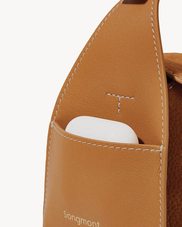 Mini Drippy Roof Bag in Sea Buckthorn nubuck leather with a white earbud case in the front pocket. Features debossed Songmont logo.