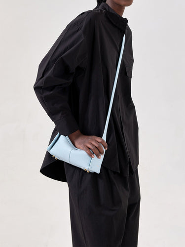 Light blue full-grain leather Mini Drippy Roof Bag with gold hardware, worn crossbody.