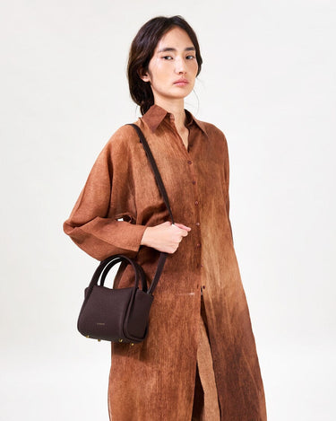 Burgundy Mini Song Bag with gold hardware carried by a woman in a brown ombre dress
