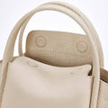 Close-up of the ivory Mini Song Bag, showcasing its textured full-grain leather, rounded handles, and structured opening.