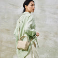 Mini Song Bag in Ivory leather, a small pebble-grain bucket bag with double handles and shoulder strap on a model.