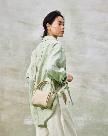 Mini Song Bag in Ivory leather, a small pebble-grain bucket bag with double handles and shoulder strap on a model.