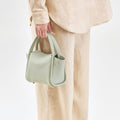 Mini Song Bag in Jade pebble leather, a compact bucket bag with gold hardware, held by a person in beige linen clothing.