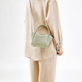 Jade Mini Song Bag with top handle and gold hardware, worn crossbody by a person in beige linen clothing.