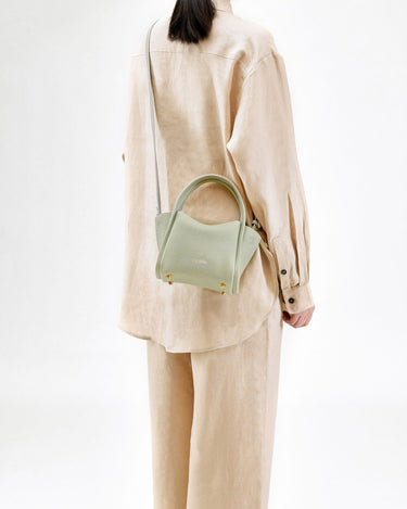 Jade Mini Song Bag with top handle and gold hardware, worn crossbody by a person in beige linen clothing.