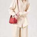 Red Mini Song Bag made of textured leather with gold hardware, worn by a model in a cream linen outfit.