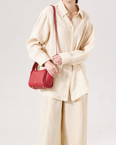 Red Mini Song Bag made of textured leather with gold hardware, worn by a model in a cream linen outfit.