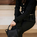 Black Mini Song Bag in textured leather with gold hardware, held by a person in black attire.