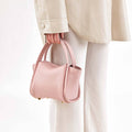 Pink full-grain leather Mini Song Bag with gold hardware, held by a hand.