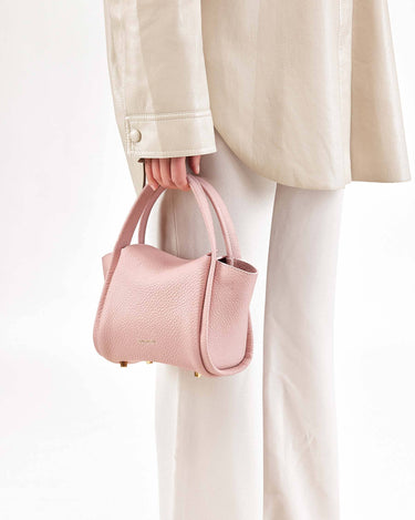 Pink full-grain leather Mini Song Bag with gold hardware, held by a hand.