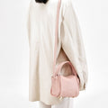 Pink Mini Song Bag with top handles and adjustable strap, worn by a model in a cream jacket.