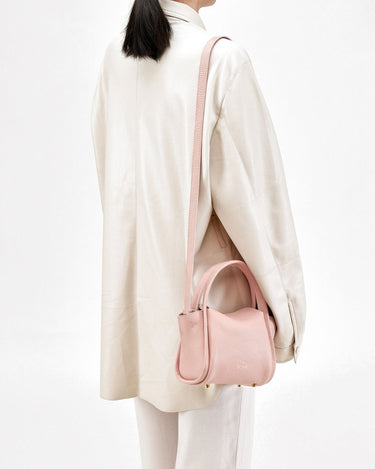 Pink Mini Song Bag with top handles and adjustable strap, worn by a model in a cream jacket.